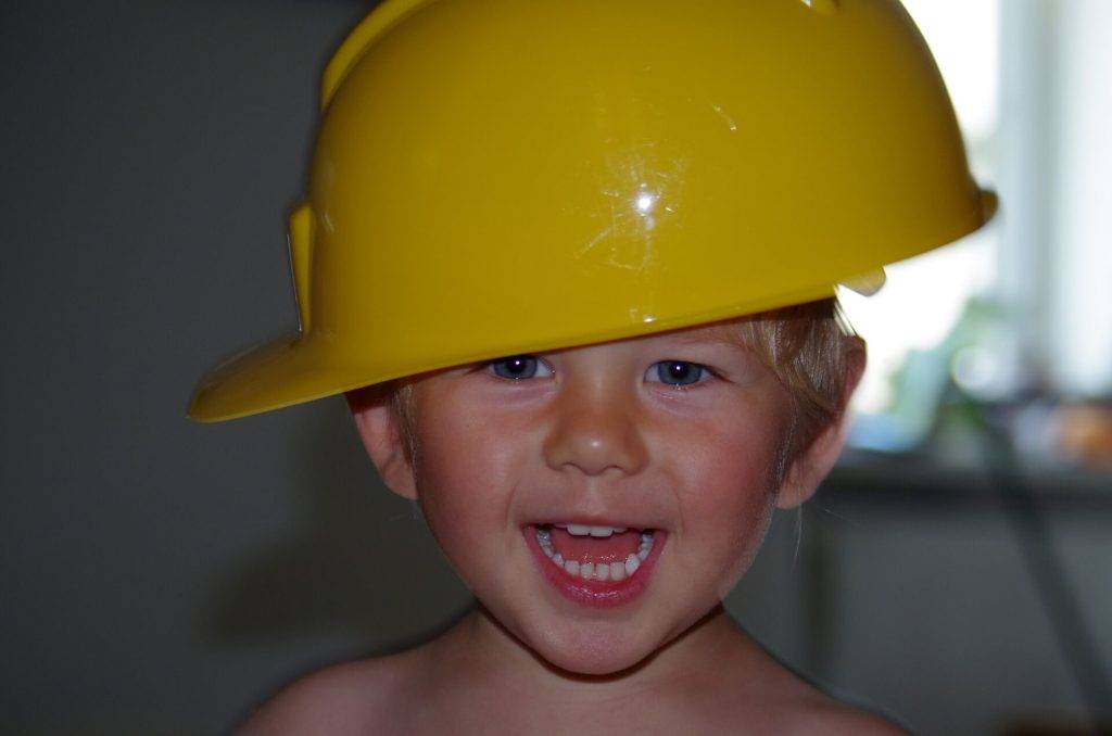 Ein kleiner Junge traegt einen gelben Sicherheitshelm quer auf dem Kopf.